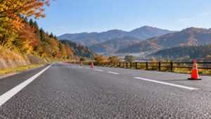 秋の山並みと交通コーンのある道路のAI生成イメージ
