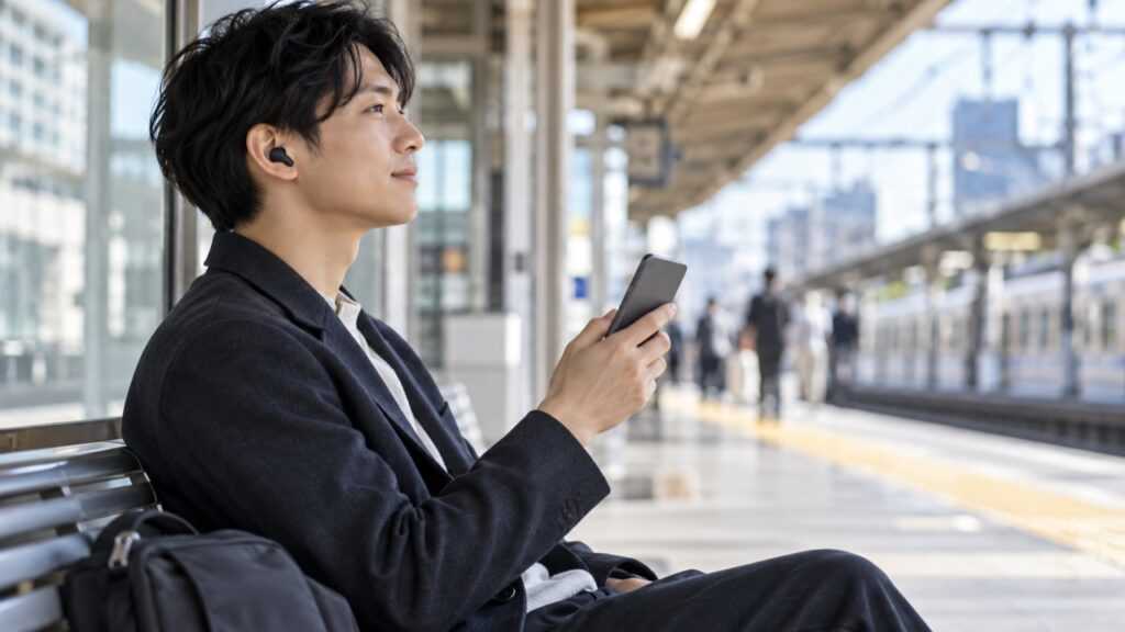 駅の待合でワイヤレスイヤホンを使って音楽を聴くイメージ